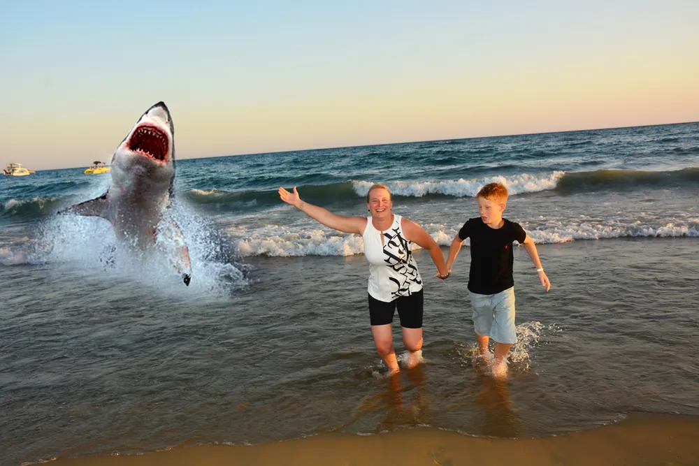 Kreative Montage: Familie am Strand mit springendem Hai