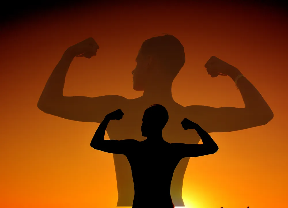 Silhouette in Muskel-Pose vor orangem Sonnenuntergang