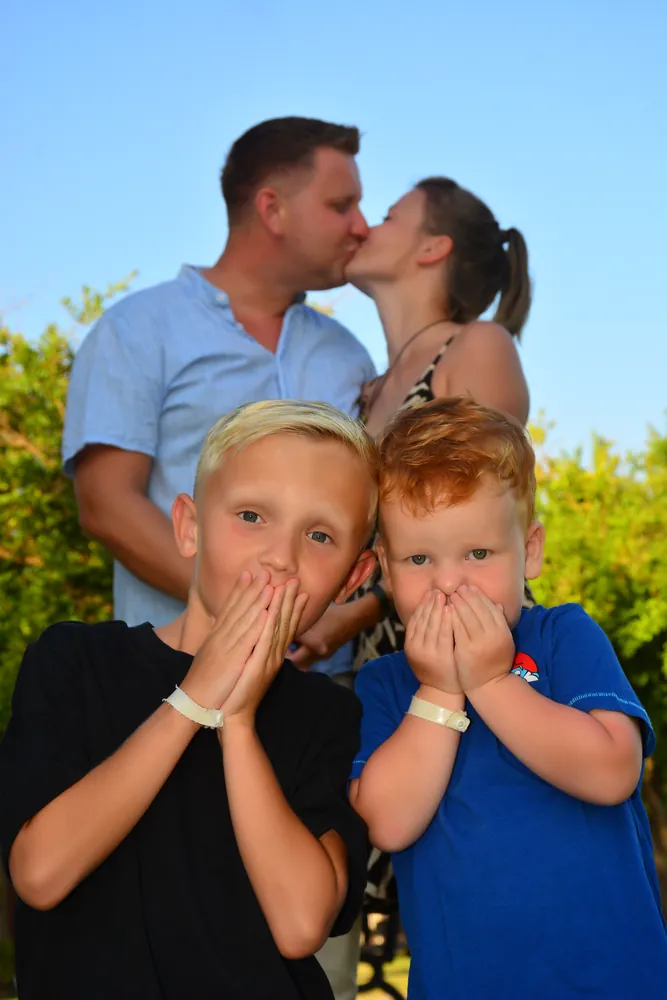 Eltern küssen sich, die Kinder halten sich die Augen zu