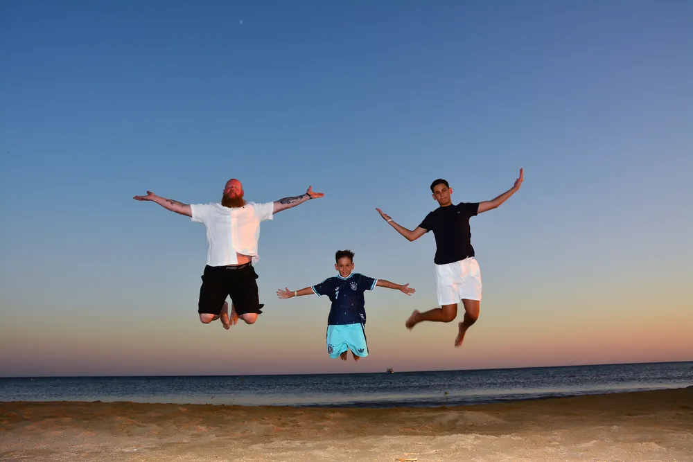Vater und Söhne springen gemeinsam am Strand in die Luft