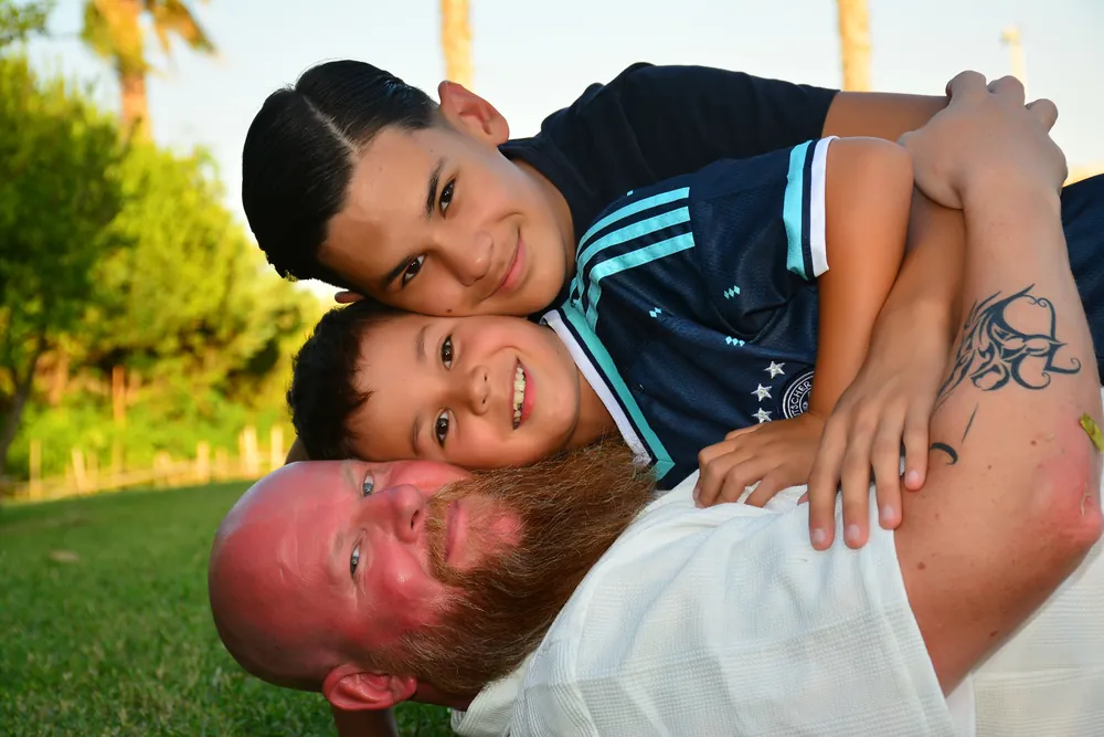 Vater und Söhne übereinander im Gras, alle lachen