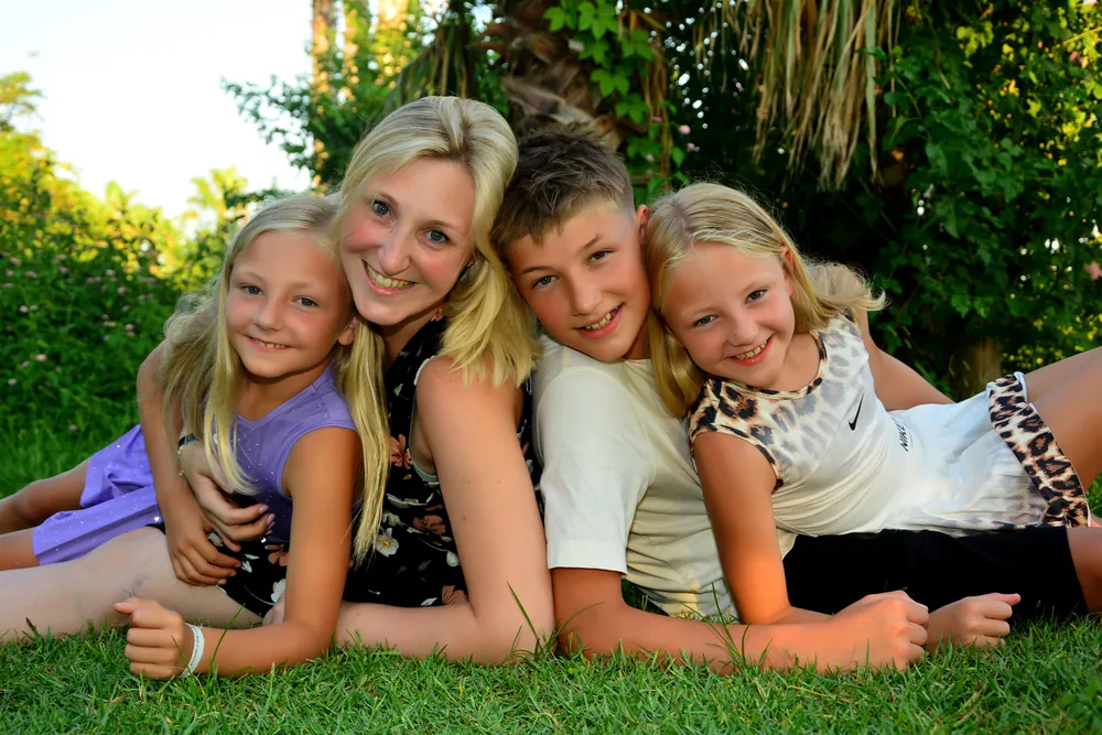 Mutter mit ihren drei Kindern lachend im Gras liegend