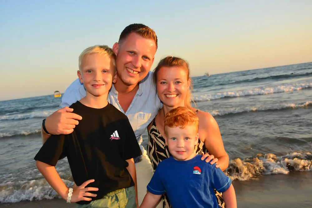 Familie zu viert am Strand vor Sonnenuntergangshimmel