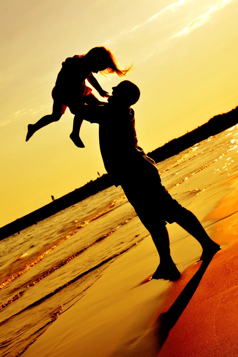 Vater wirft sein Kind lachend in die Luft, Strandsilhouette im Sonnenuntergang