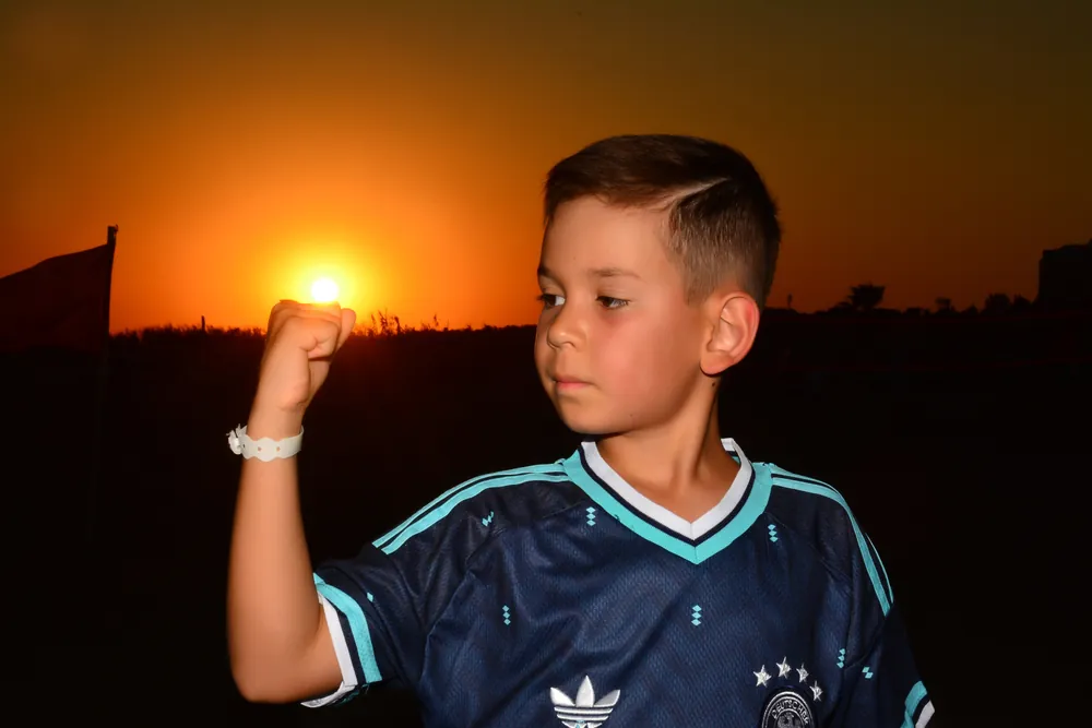 Junge hält die untergehende Sonne in der Hand